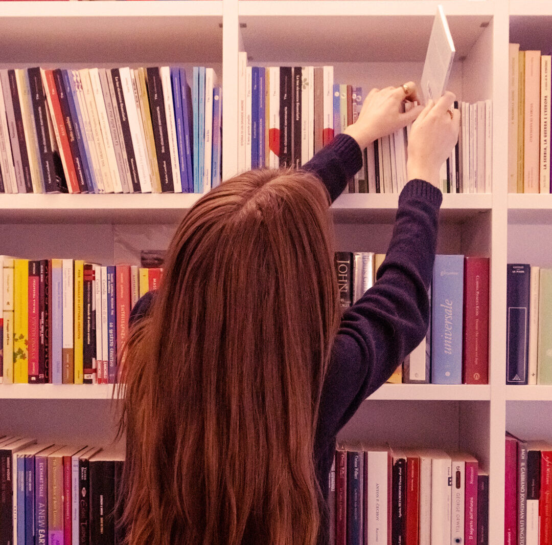 ragazza di spalle prende un libro da una libreria"